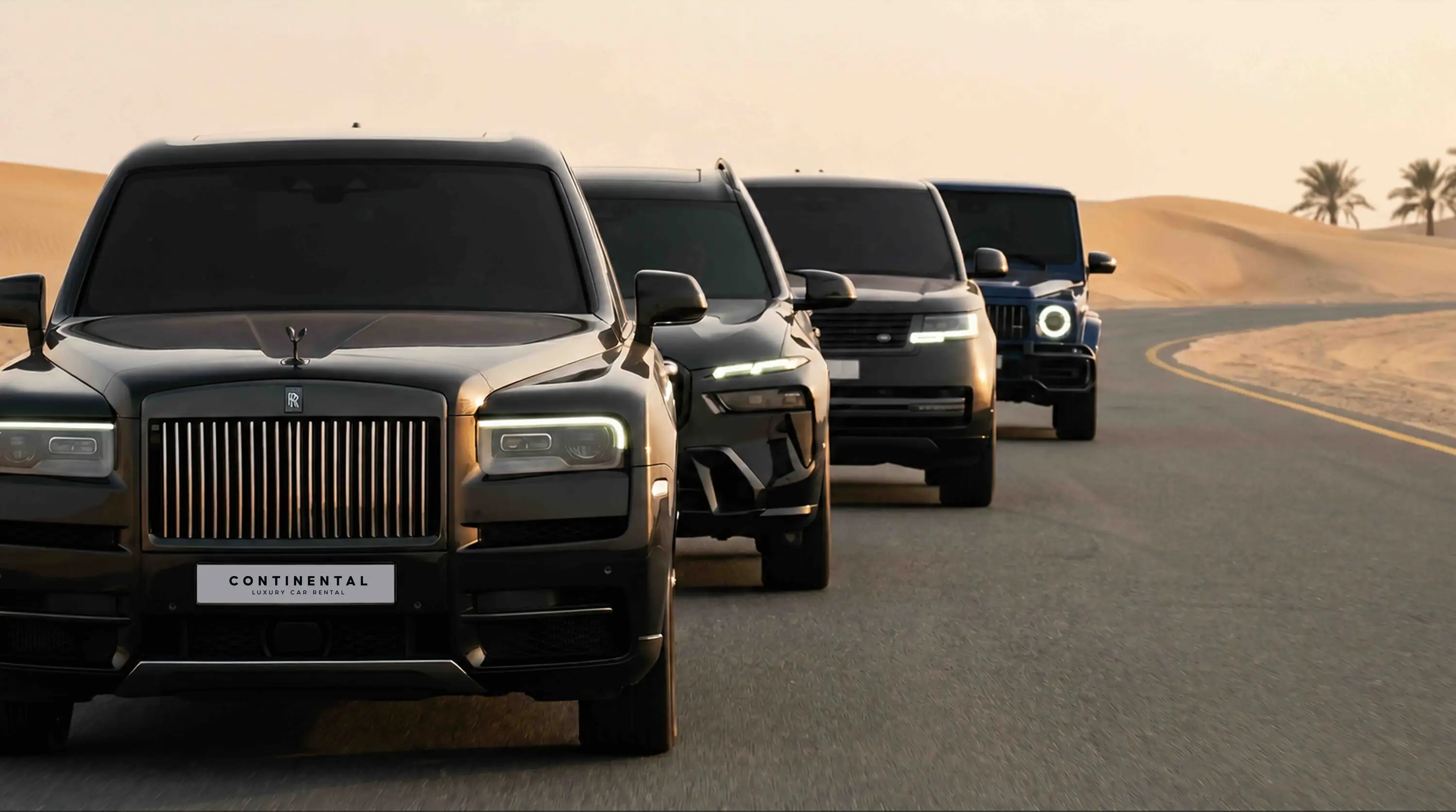A black Rolls-Royce Cullinan with a CONTINENTAL Luxury Car Rental plate leads a convoy of SUVs along a desert road at dusk